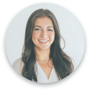 The image is a portrait of a woman smiling warmly at the camera. She has long brown hair and is wearing a white shirt. The photo is framed within a circular border, and her expression conveys a friendly, approachable demeanor.